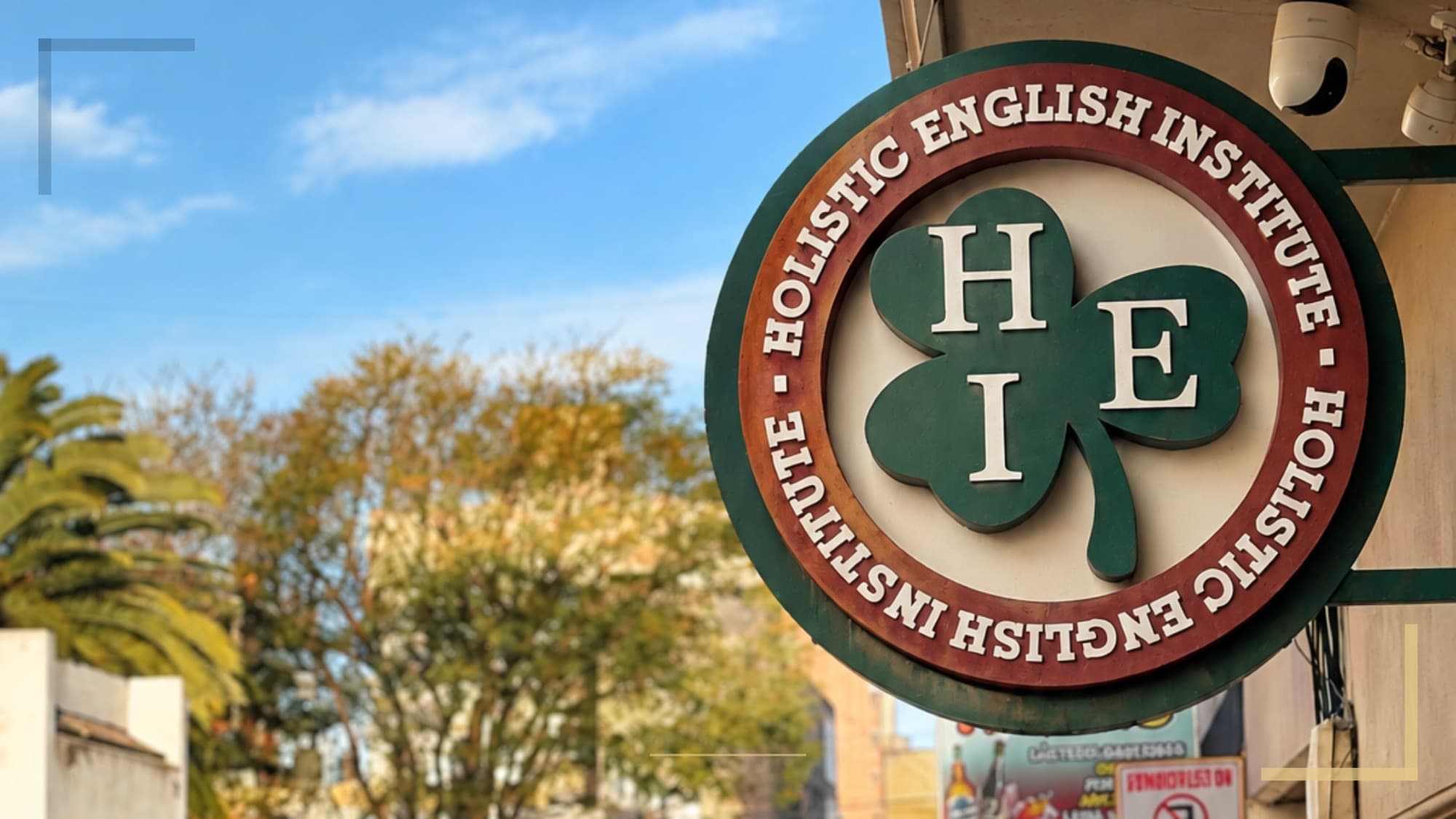 Cartel circular del Holistic English Institute, con el trébol verde y las letras HEI, en el frente del instituto.